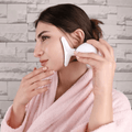 Woman using a facial massager for skin rejuvenation and lifting, wearing a soft pink bathrobe.